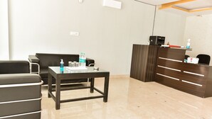 A modern reception area with a dark wooden desk, a glass-top table, and a leather sofa. - Hotel Blue Saffron (New Delhi)