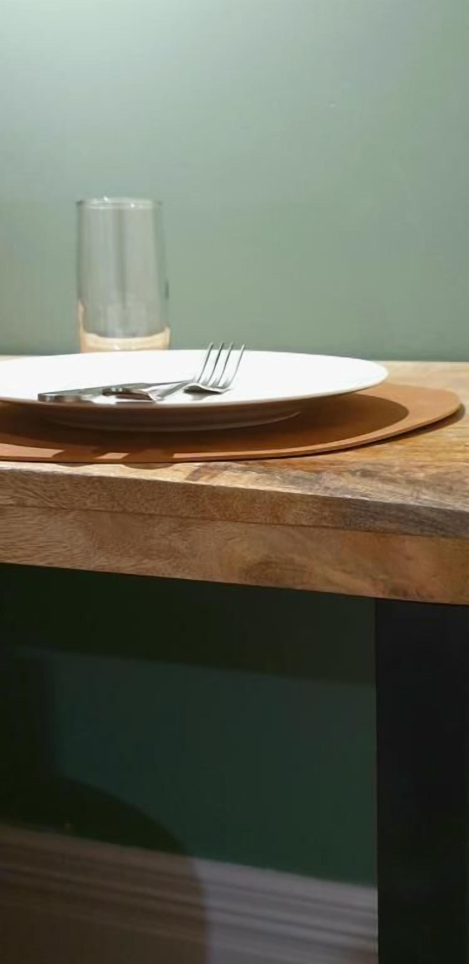 A dining table with a plate, fork, and knife set on a wooden table.