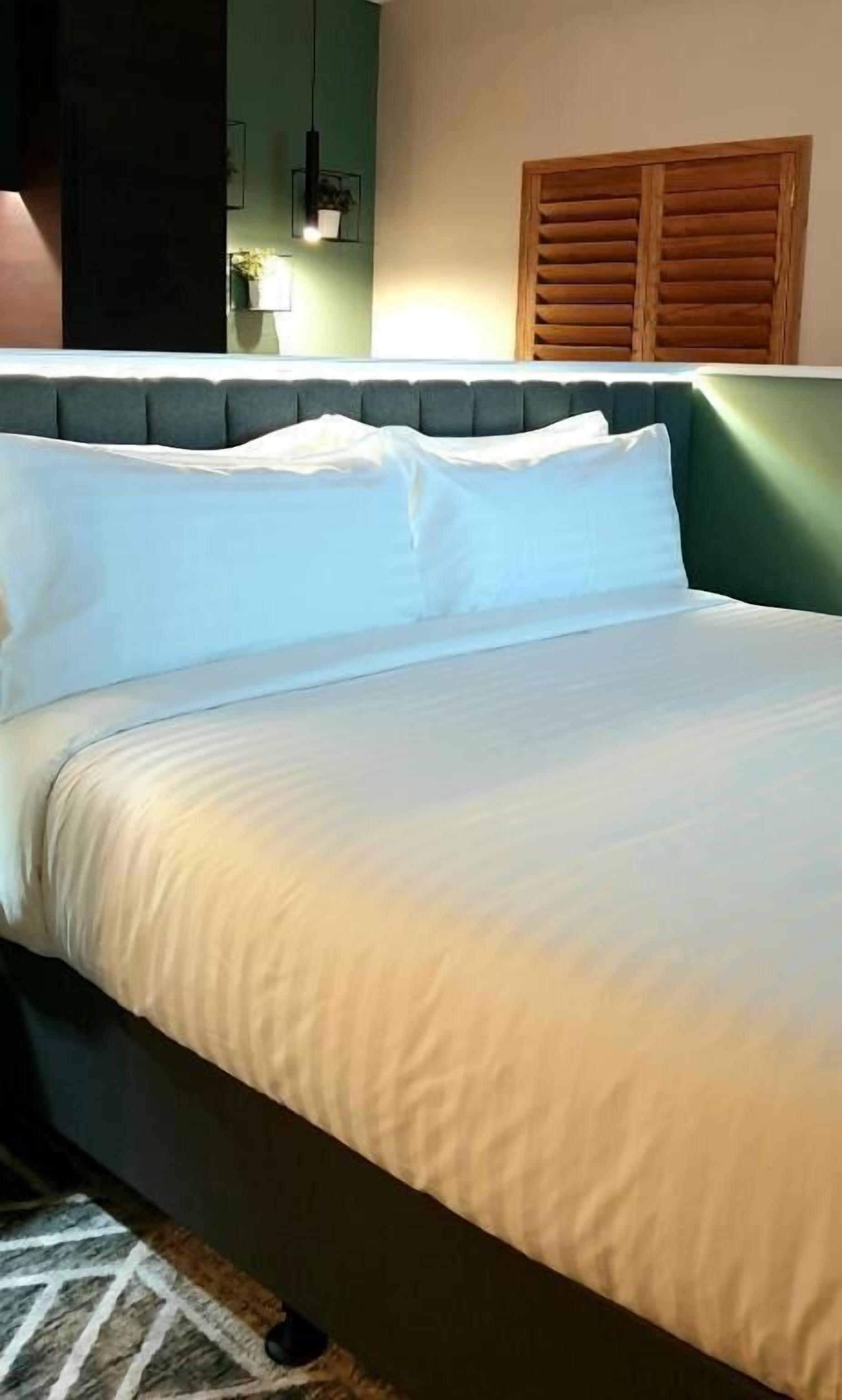 A bed with white bedding, a dark headboard, and a green wall with a wooden panel.