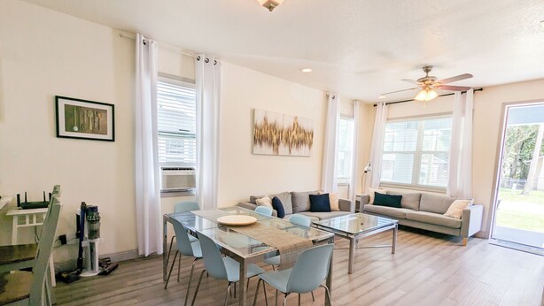 A modern living room with a glass dining table, two sofas, and a ceiling fan.