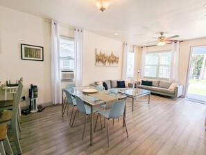 A modern living room with a glass dining table, two sofas, and a ceiling fan. - City getaway modern house (Tampa)