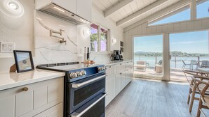 Una cocina moderna con una estufa grande, armarios blancos y vistas a un lago a través de amplias ventanas.