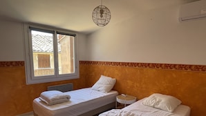 A room with two beds, a window, and a hanging light fixture. - House in the heart of the village (Montagnac)