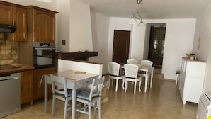 A kitchen with wooden cabinets, a built-in oven, and a dining area with a table and chairs. - House in the heart of the village (Montagnac)