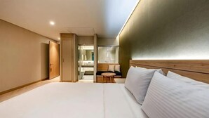 A modern hotel room with a large bed, a wooden headboard, a small seating area, and a bathroom visible through an open door. - Hotel Foret The Spa (Busan)