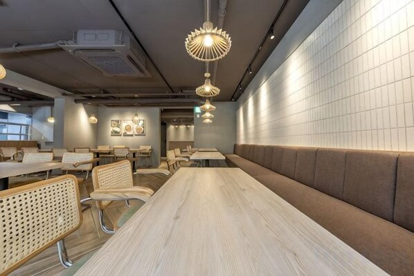 A modern dining area with a long table, cushioned seating, and pendant lighting.