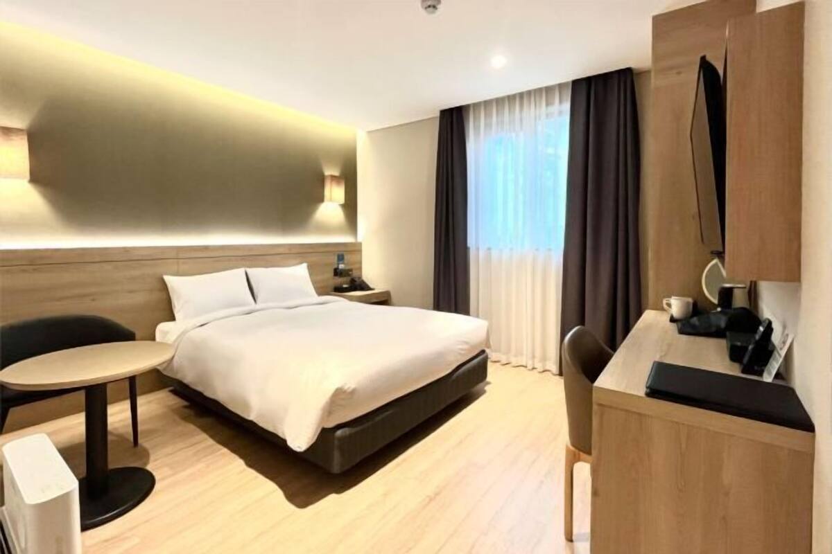 Ein Hotelzimmer mit Bett, Schreibtisch, Stuhl, Nachttisch und Fernseher.