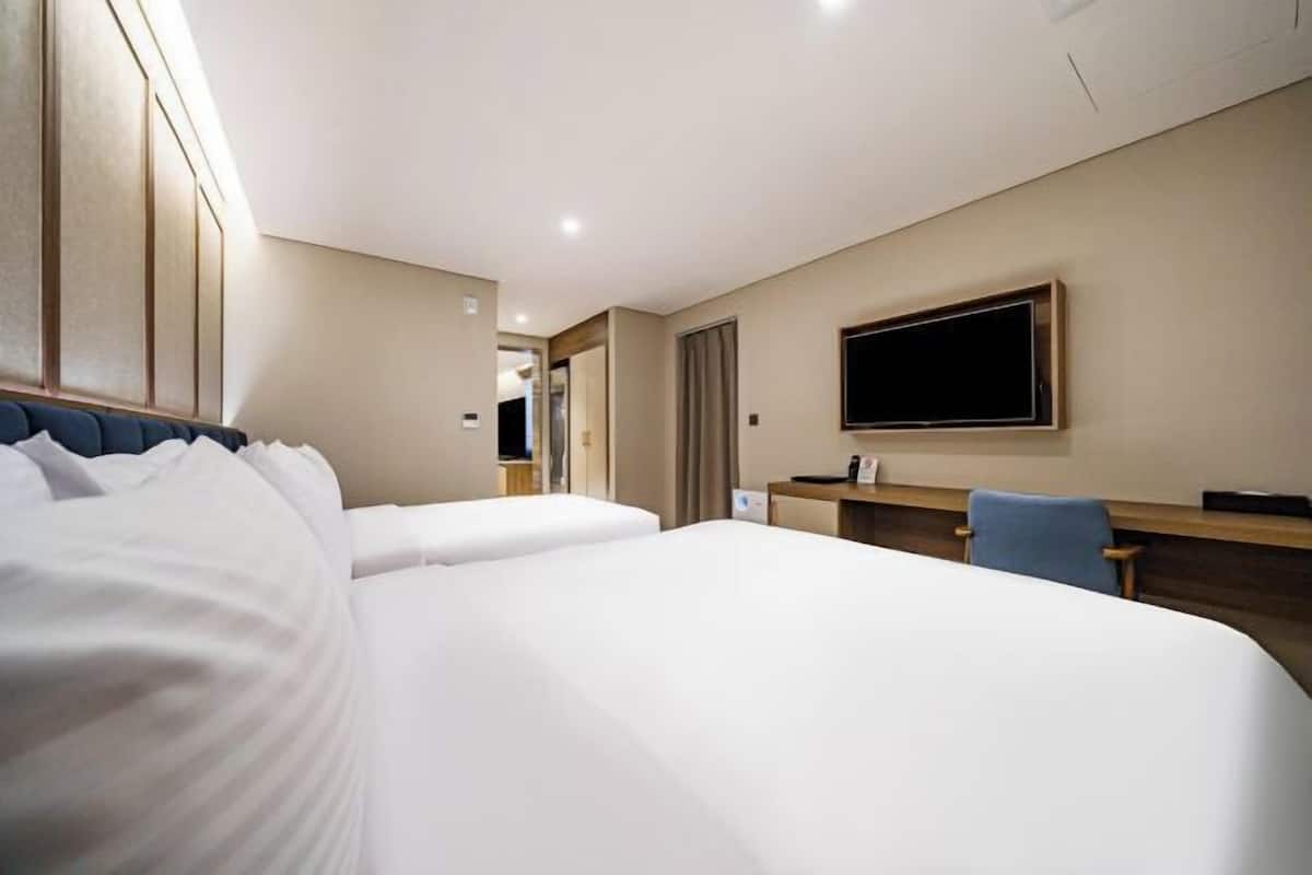 Ein Hotelzimmer mit zwei Betten, einem Schreibtisch, einem Stuhl, einem Fernseher und einem Spiegel.
