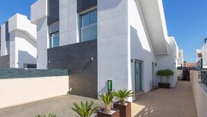 Um edifício moderno com telhado plano, grandes janelas e um pequeno pátio com plantas em vasos.