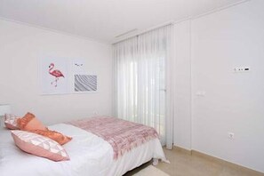 Une chambre à coucher avec un lit, une fenêtre ornée de rideaux légers et un mur sur lequel sont accrochées deux images encadrées.