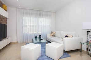 Un salon moderne avec un canapé blanc, une table basse en verre et un téléviseur à écran plat fixé à un mur en briques.