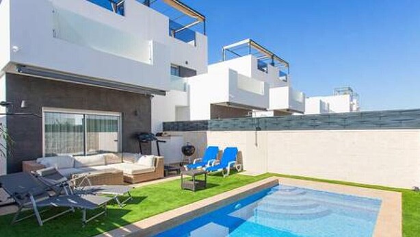 Um edifício moderno de dois andares com piscina, área de estar ao ar livre e céu azul claro.