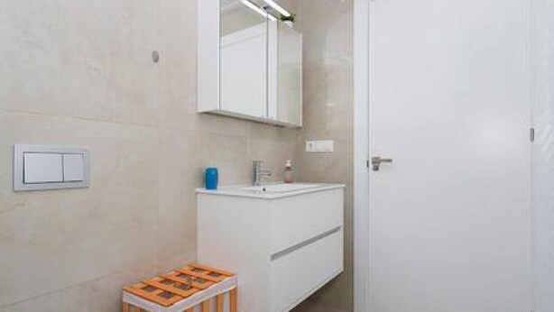 Een badkamer met een wit wastafelmeubel, een spiegel erboven en een deur aan de rechterkant.