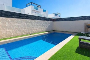 Une piscine dotée d’une terrasse carrelée, entourée d’un petit muret et d’une zone herbeuse.