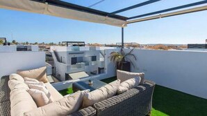 Um terraço no telhado com um sofá de vime, uma mesa pequena e um vaso com planta.