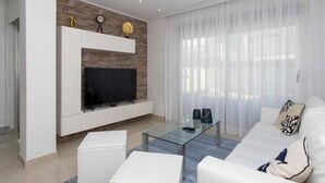 Uma sala de estar moderna com uma televisão de tela plana, uma mesa de centro de vidro e um sofá branco.