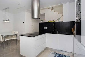 Une cuisine moderne avec des meubles blancs, un plan de travail noir et une hotte en acier inoxydable.
