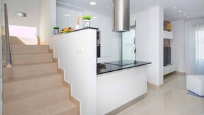 Uma cozinha moderna com ilha central, coifa de aço inoxidável e escada para um andar superior.