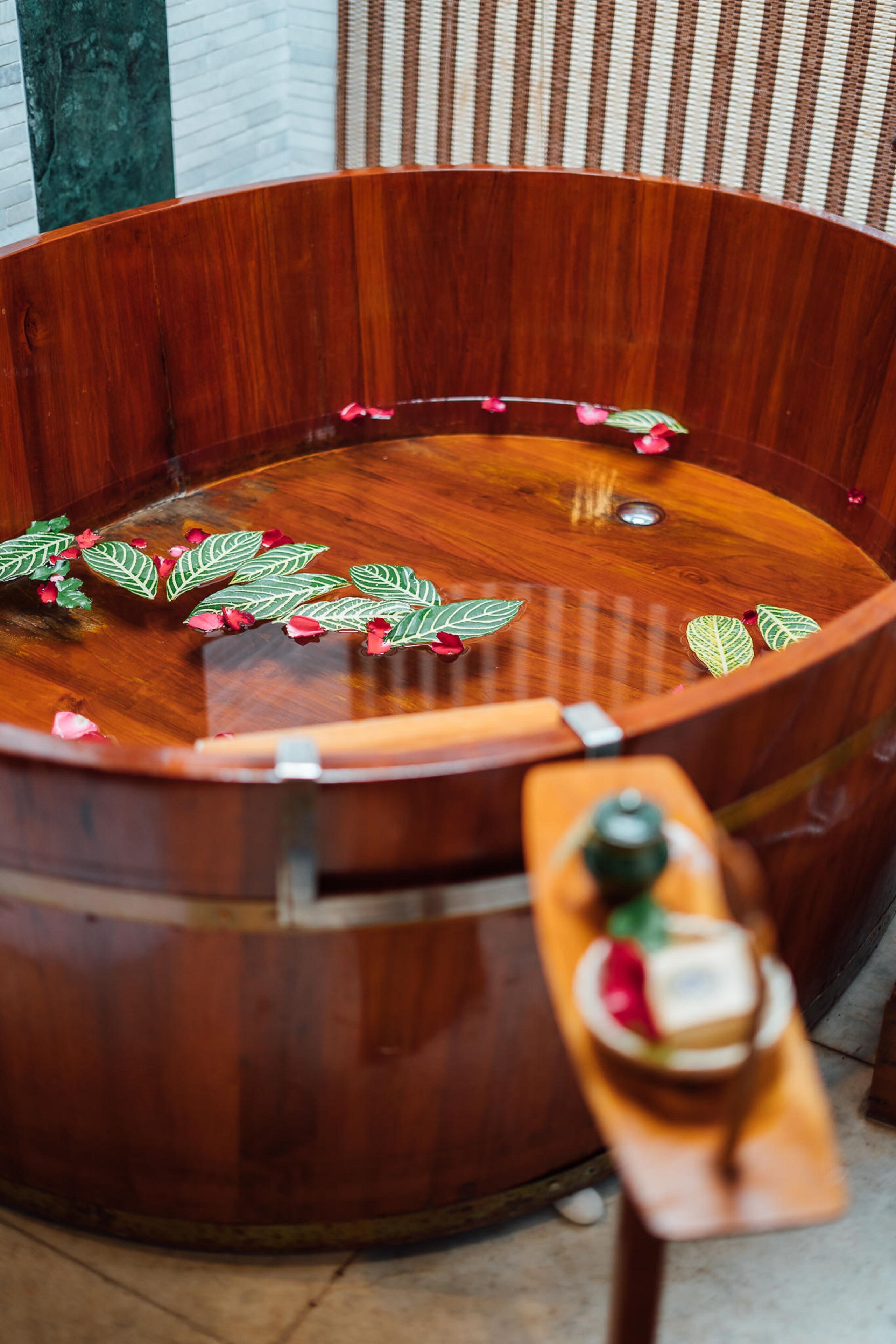 Une baignoire en bois avec un banc en bois, entourée de feuilles et de fleurs décoratives.