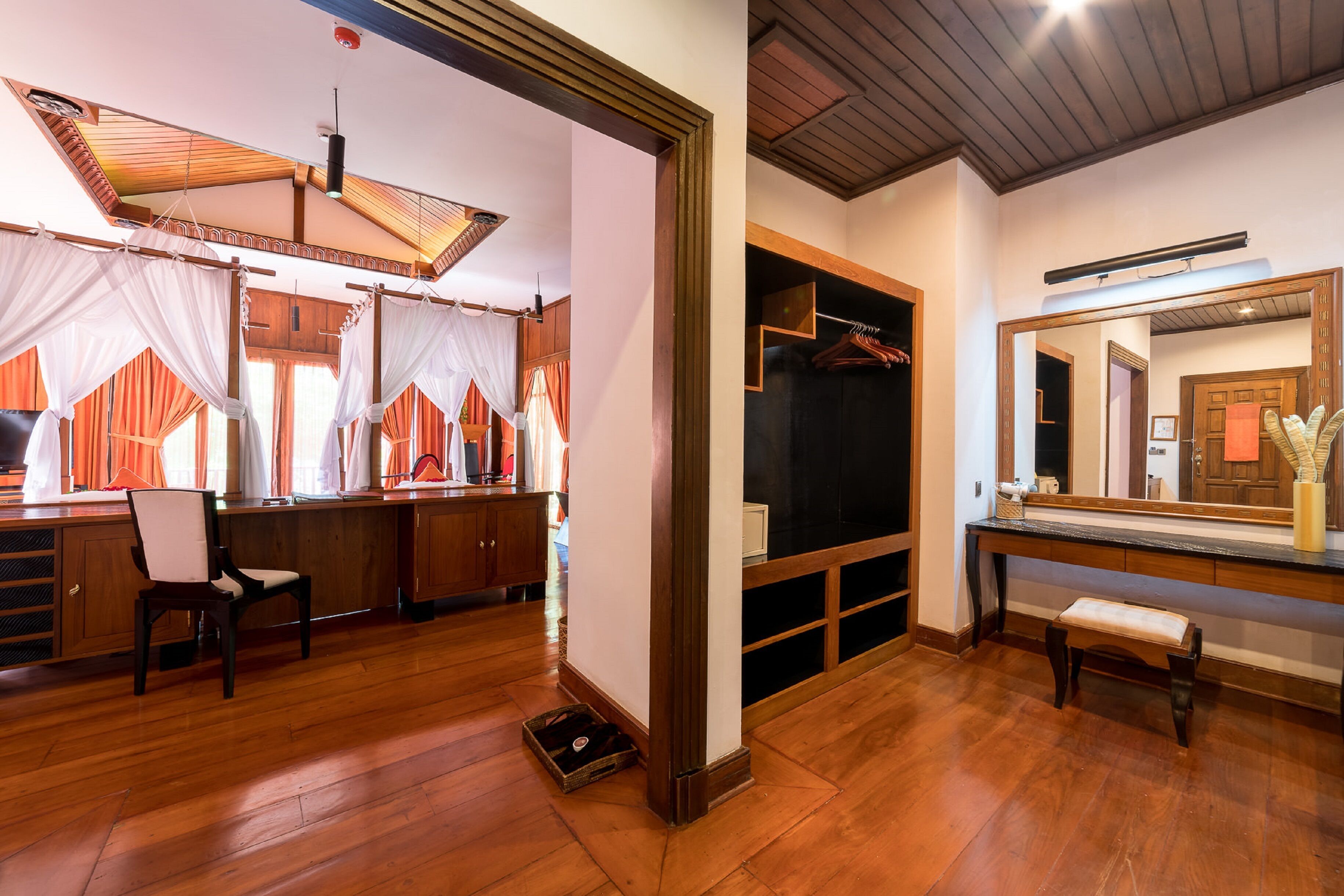 A room with a wooden floor, a bench, a mirror, and a wardrobe with hanging clothes.