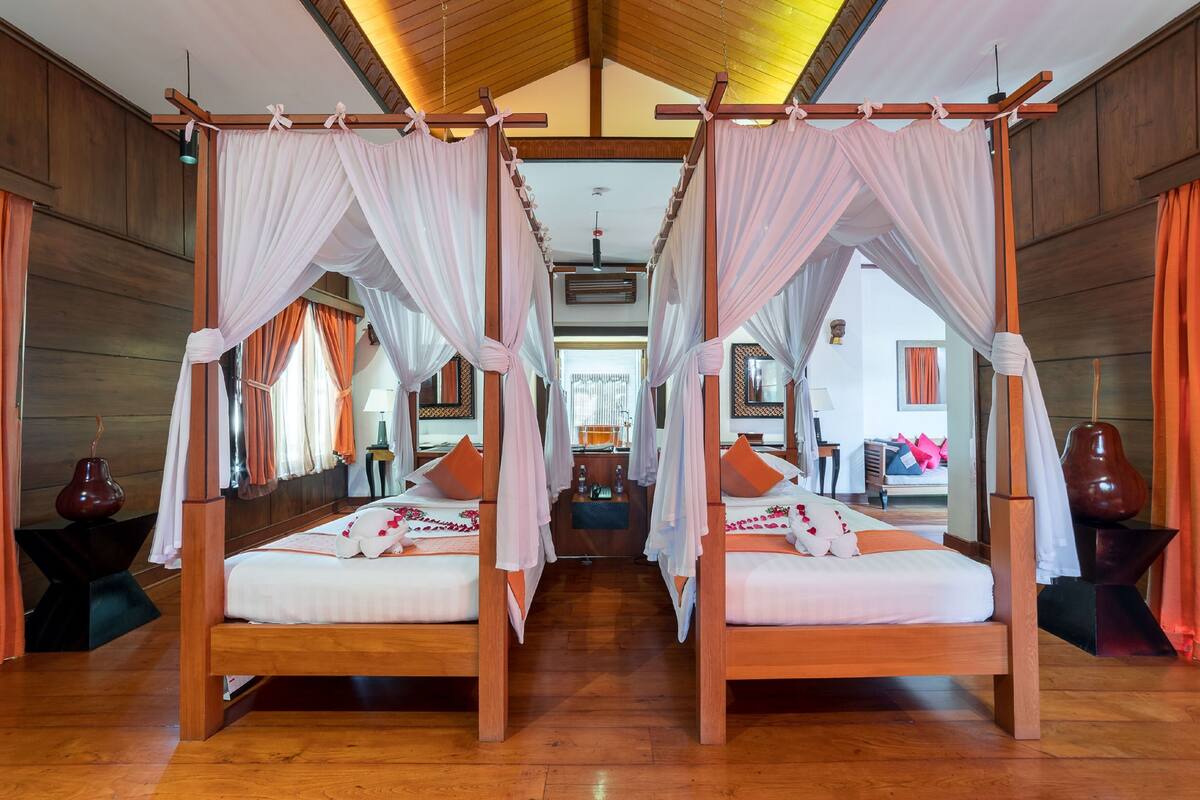 Ein Zimmer mit zwei hölzernen Betten mit Baldachin, jeweils mit weißer Bettwäsche und orangefarbenen Kissen.