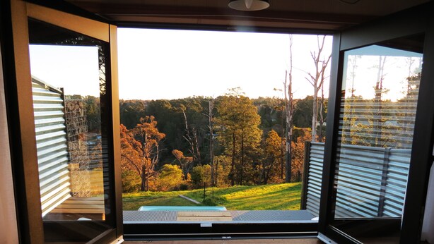 A room with a large sliding glass door leading to a view of a green landscape with trees and a clear sky. - Sleep in the Clouds! The Haiku Hut... (Wentworth Falls)