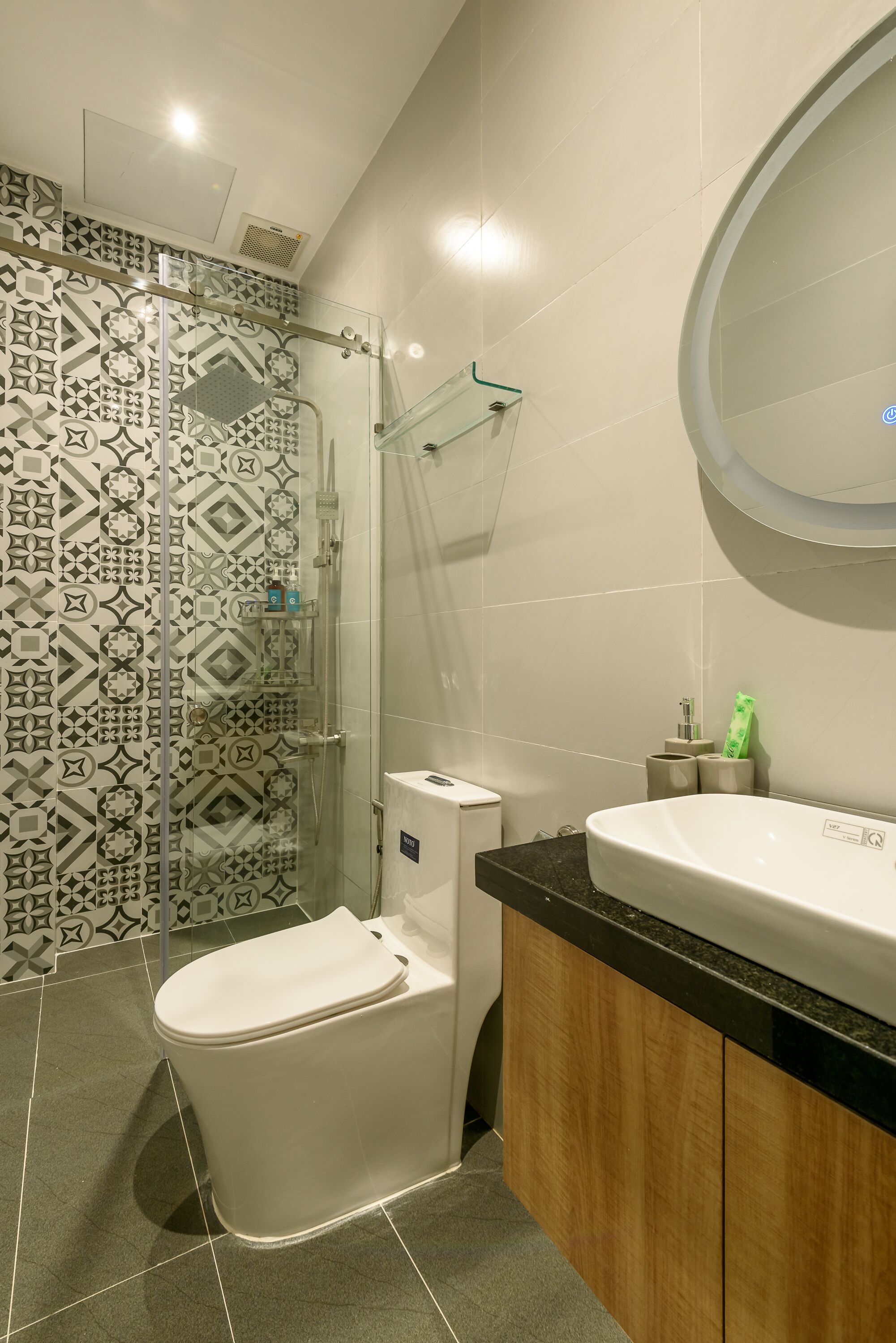 Een moderne badkamer met een betegelde douchewand, een douche met glazen wanden, een wit toilet en een wastafel met spiegel.
