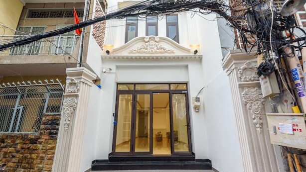 Un immeuble à la façade blanche, doté d’une grande porte d’entrée en verre et d’un balcon avec des balustrades en métal.