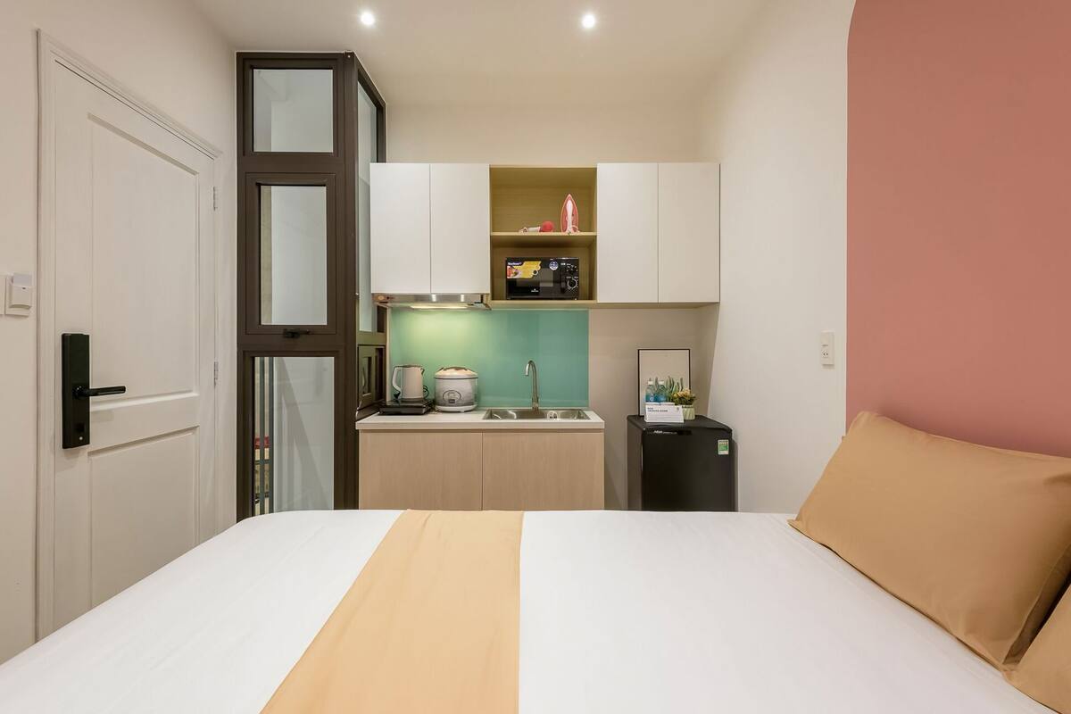 Een compacte hotelkamer met een bed, een kitchenette, een kleine koelkast en een deur.