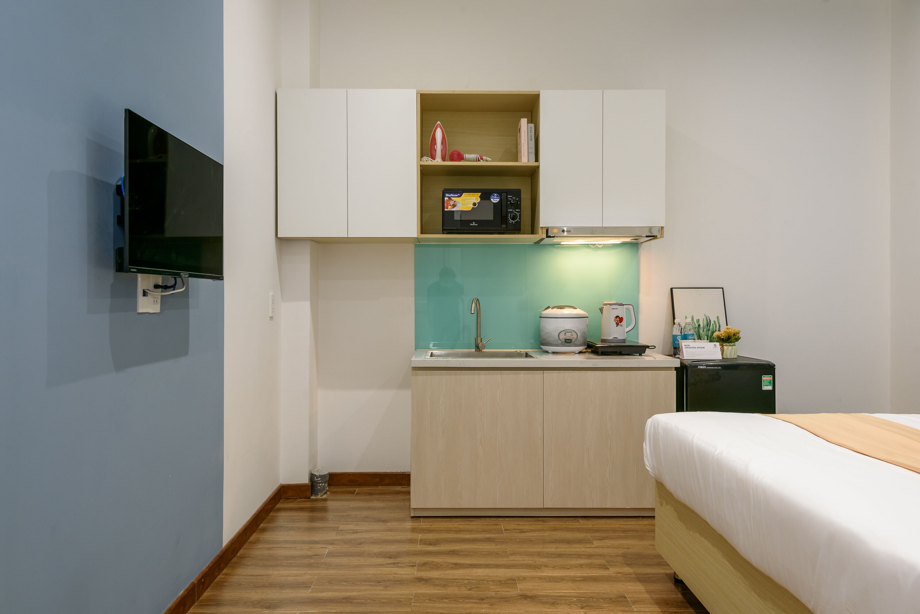 Ein kleines Hotelzimmer mit Küchenzeile, einem Bett und einem an der Wand befestigten Fernseher.