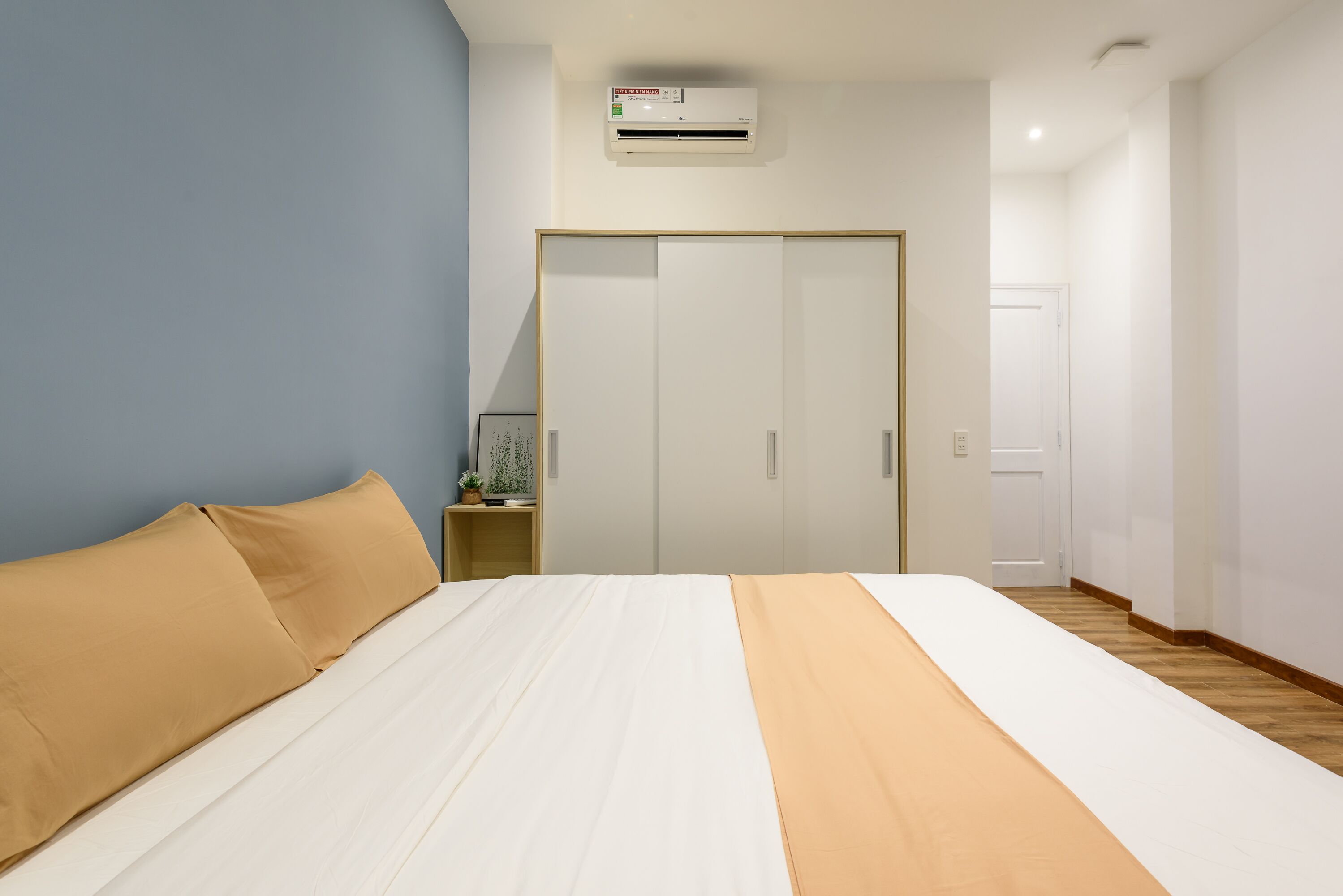 A bedroom with a bed, a wardrobe, an air conditioning unit, and a nightstand with a lamp.