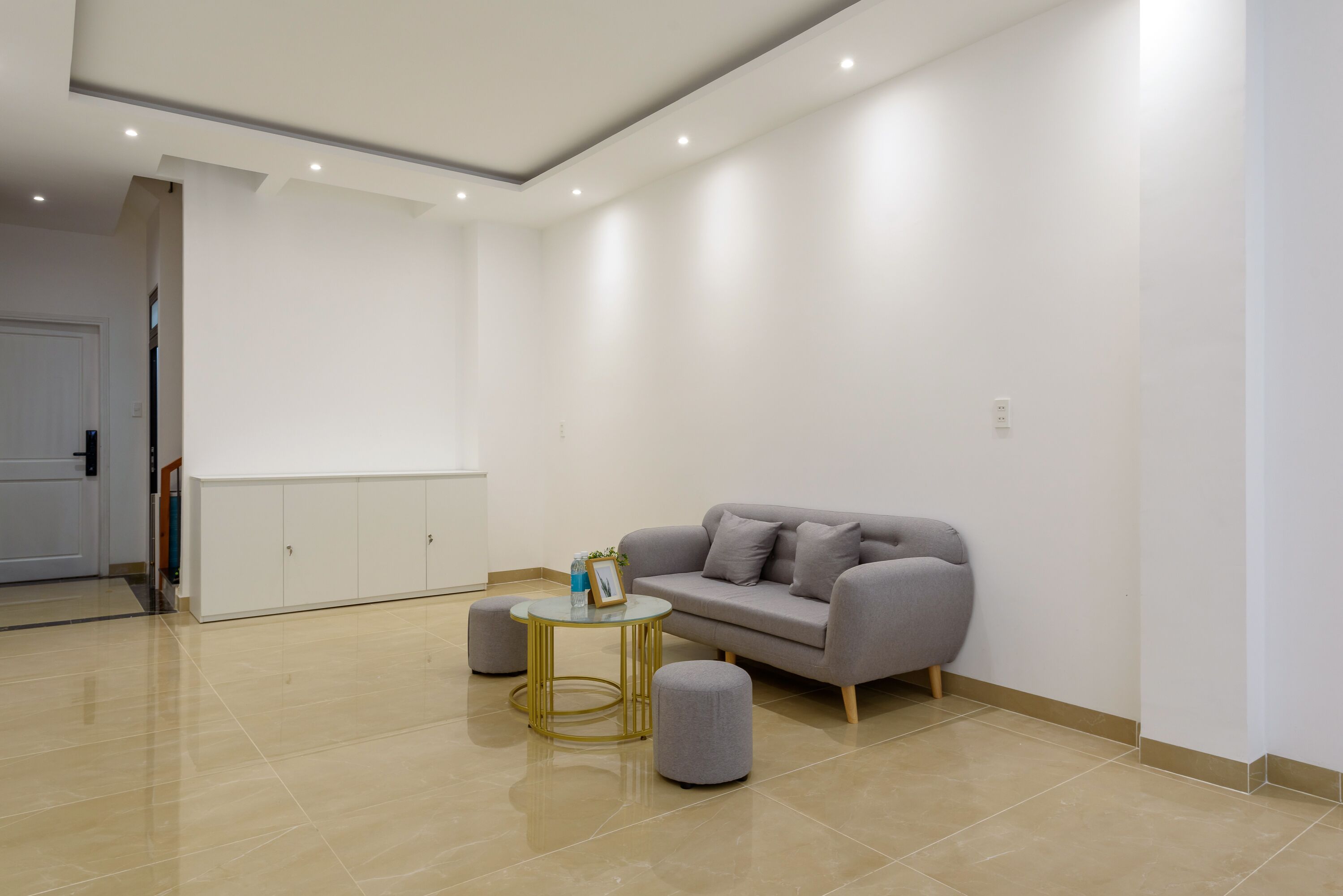 Ein modernes Wohnzimmer mit einer grauen Couch, zwei Poufs, einem runden Couchtisch und einem Schrank.