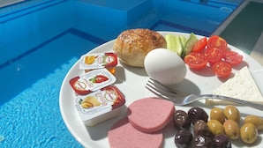 A dining table with a plate of food, a pool, and a building in the background. - Respect Apart Hotel (Alanya)