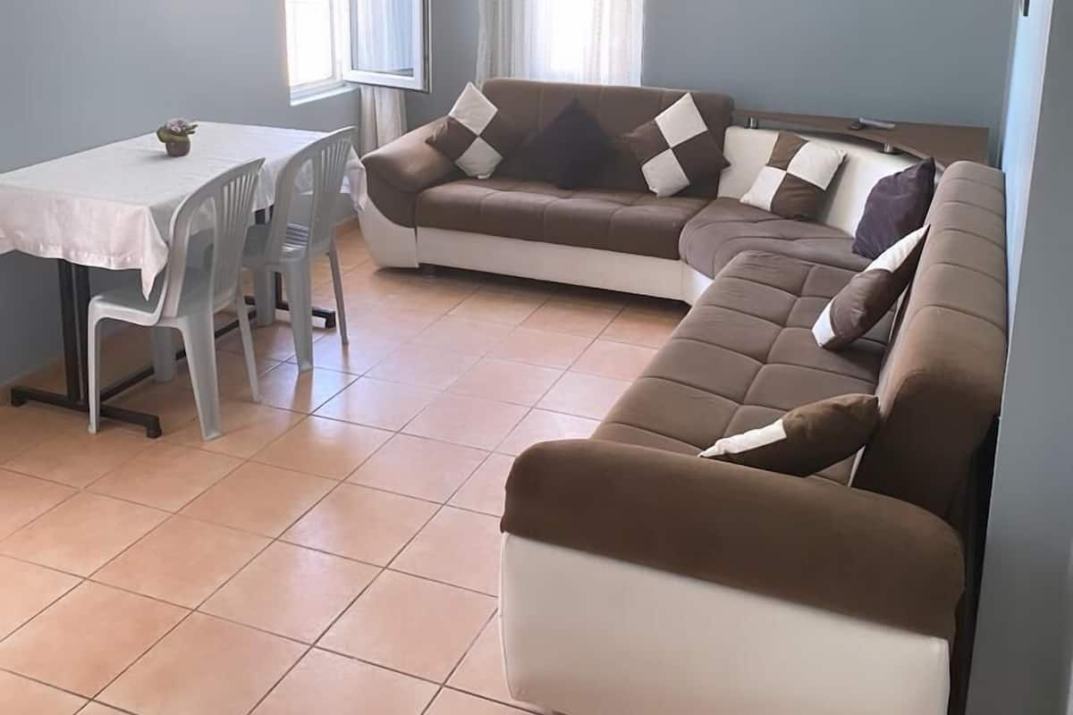 A living room with a sofa, a dining table with chairs, and a window with curtains.
