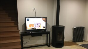 A living room with a flat-screen TV on a stand, a black wood-burning stove, and a radiator. - Gîte "La Hulotte" country property away from the city (Villeneuve-la-Lionne)