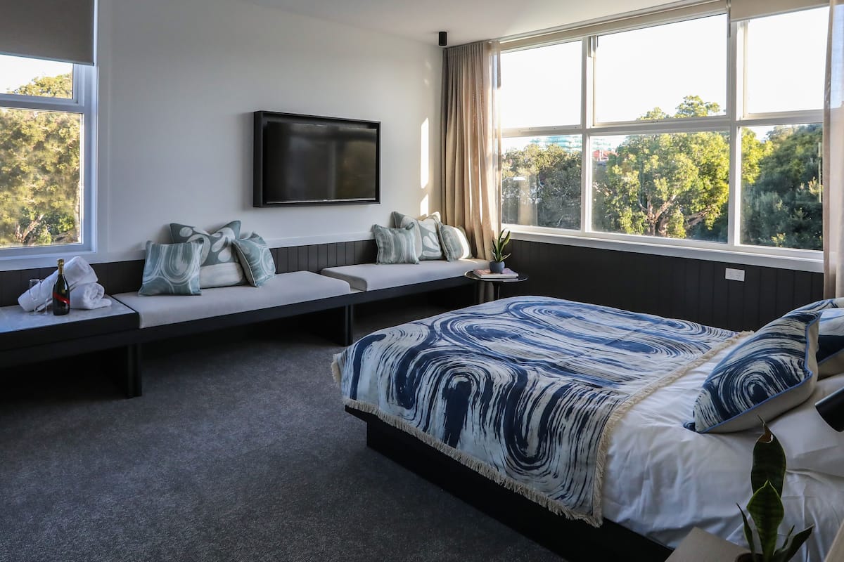 Un dormitorio con cama, sofá cama, televisión y ventana con vistas a árboles.