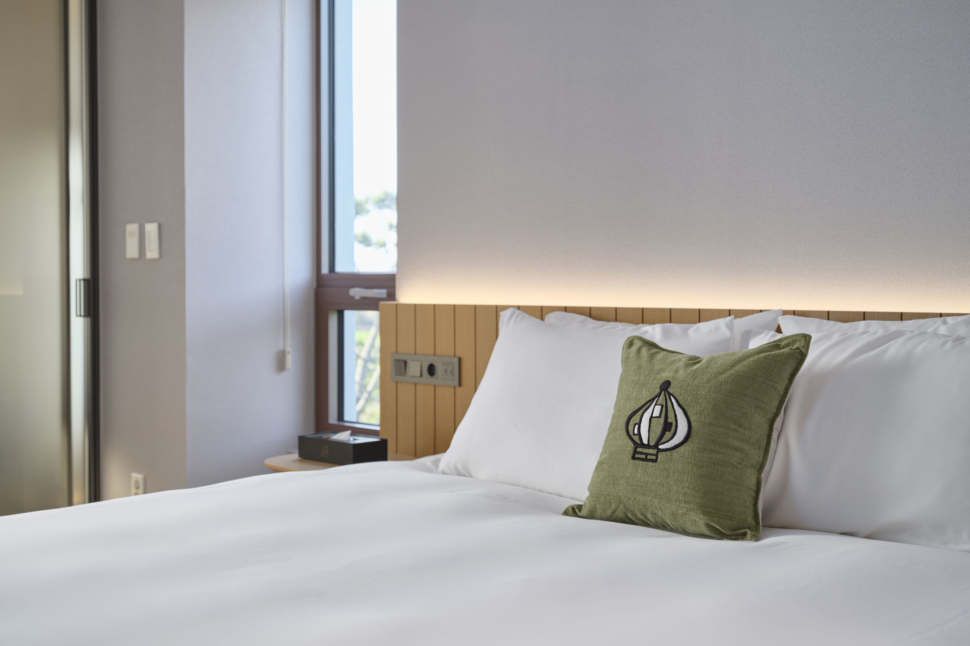 Una cama bien tendida con sábanas blancas y un cojín verde con un diseño de velero.