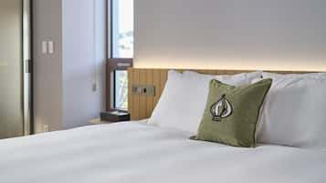 Una cama bien tendida con sábanas blancas y un cojín verde con un diseño de velero.