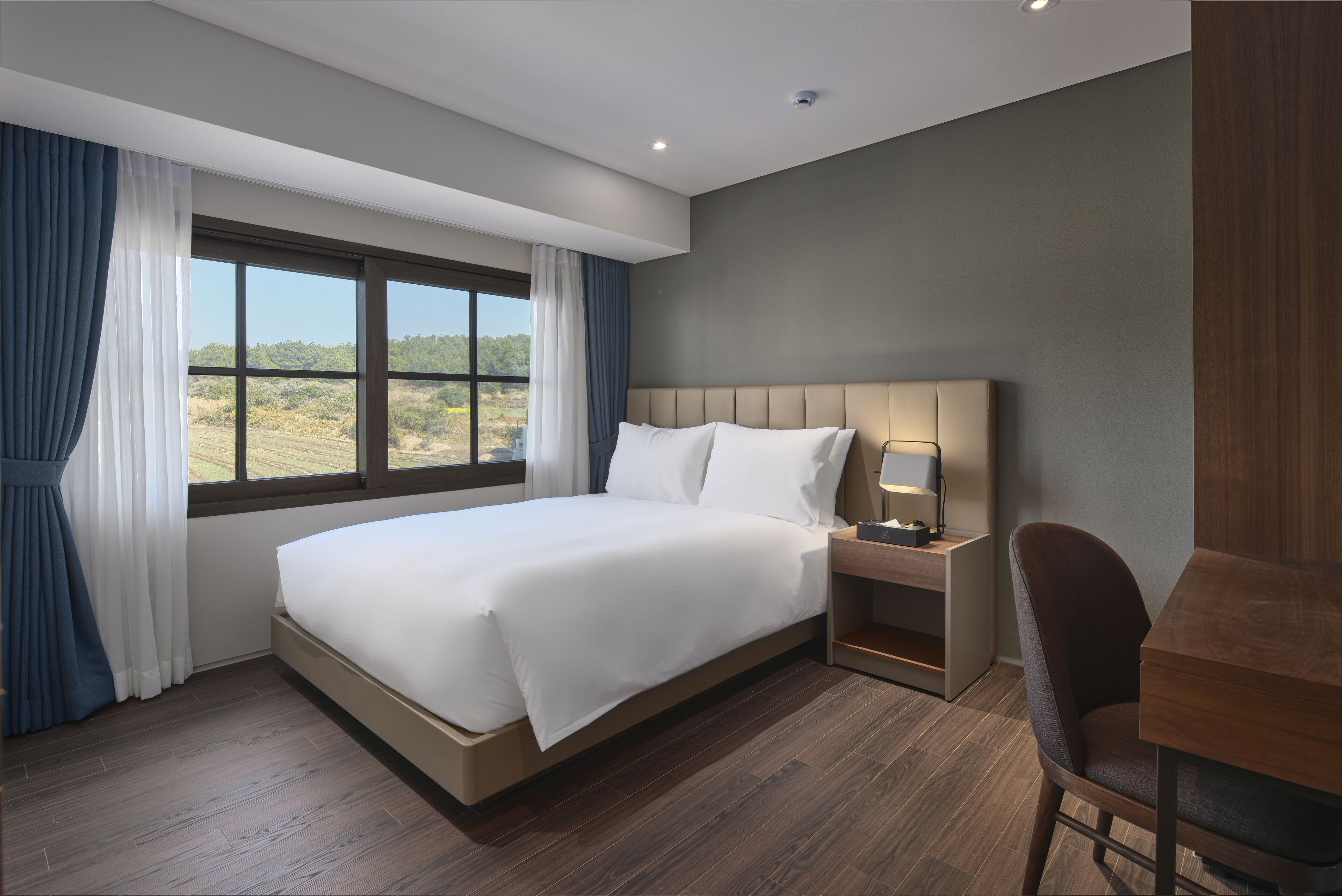 Ein modernes Hotelzimmer mit einem großen Bett, einem Nachttisch, einem Sessel und Blick ins Freie.