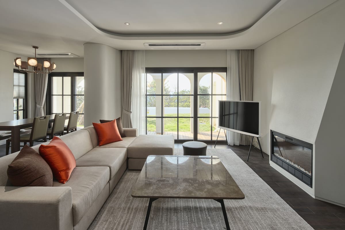 A modern living room with a sectional sofa, a glass coffee table, a flat-screen TV, and a fireplace.