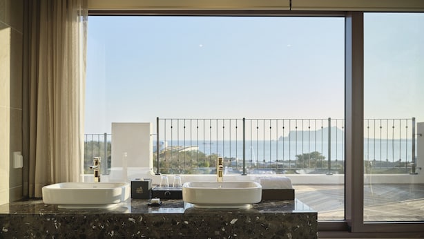 A modern bathroom with two sinks, a large window with a view of the sea, and a balcony with a railing. - Hundert Hills (Jeju City)