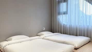 Una habitación de hotel moderna con dos camas, un ventanal con cortinas translúcidas y piso de madera clara.