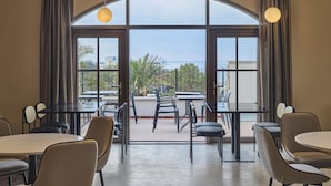 A modern dining area with glass tables and chairs, large windows with curtains, and a view of the sea. - Hundert Hills (Jeju City)