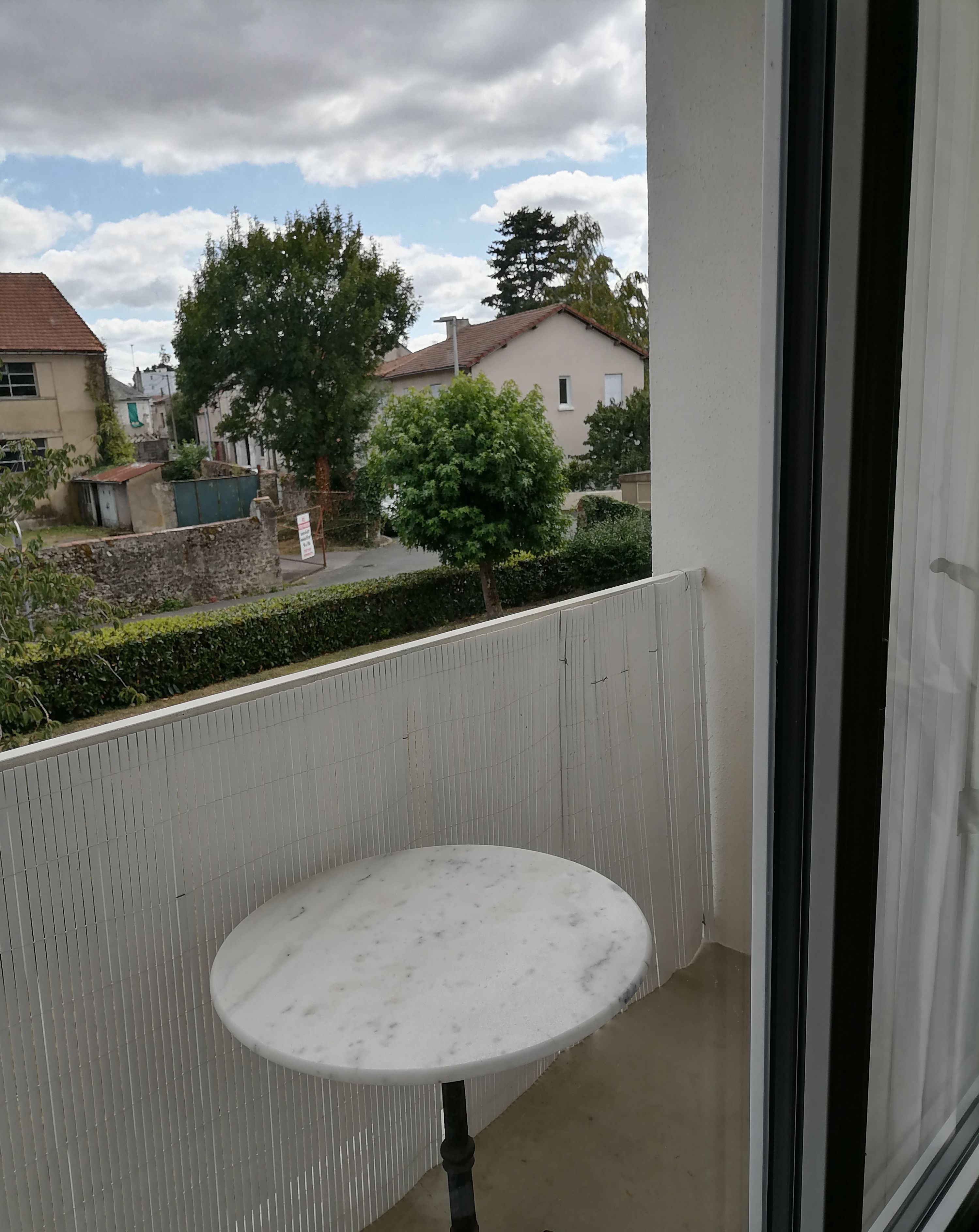 Uma varanda com uma pequena mesa redonda, vista para uma área residencial e céu claro.