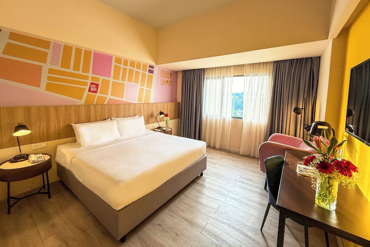 A hotel room with a large bed, a desk with a chair, a telephone, and a vase with flowers.