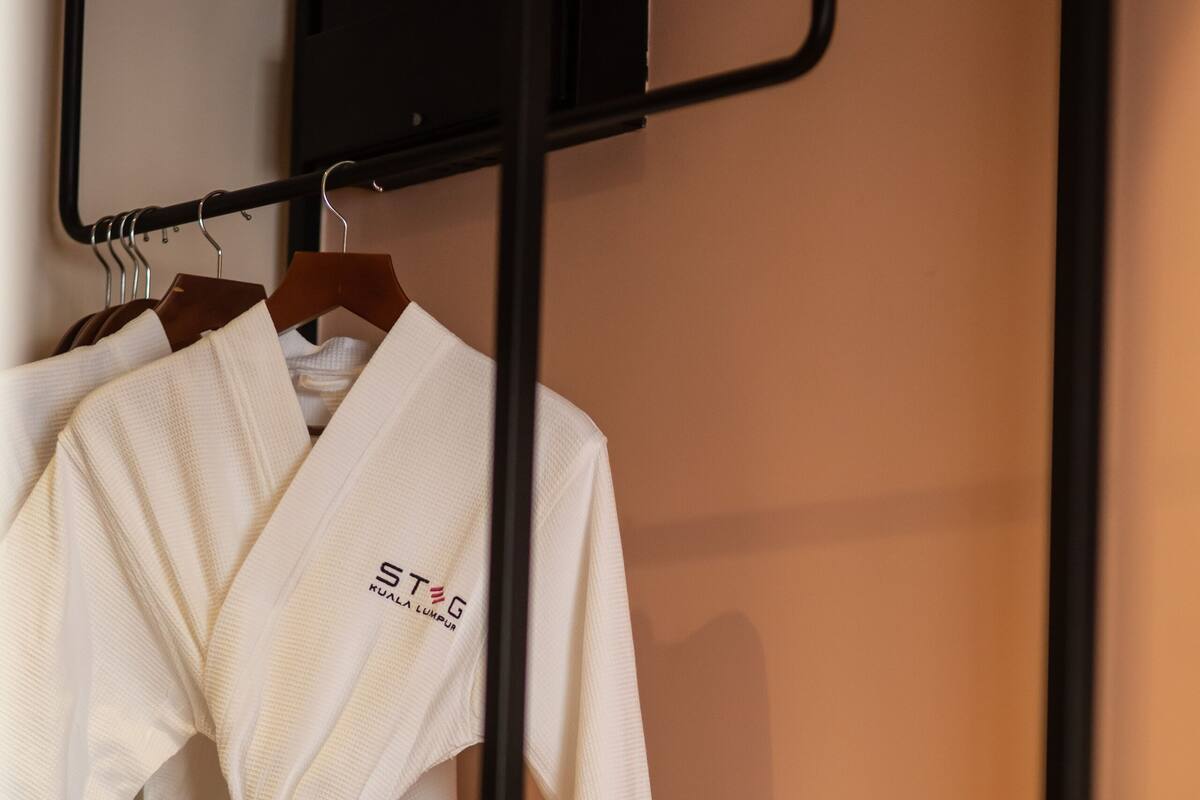 A white robe hanging on a wooden hanger in a room with a black metal rack and a wooden shelf with bottles.