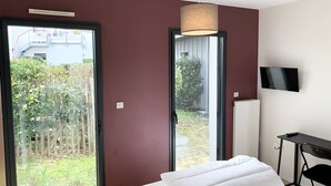 A bedroom with a bed, a TV mounted on the wall, and a door leading to a garden.