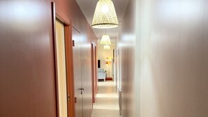 A hallway with wooden flooring, white walls, and a hanging light fixture.