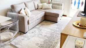 Een moderne woonkamer met een beige modulaire bank, een glazen salontafel, een kamerbreed tapijt en een houten bijzettafeltje met een kaars.