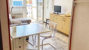 Een moderne, goed verlichte kamer met een eettafel, stoelen, een bank en een televisie.